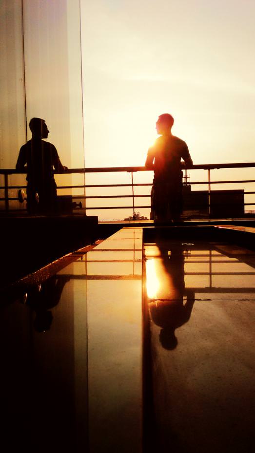 我常在生活裡攝影,也用手機拍下我重要的每一刻。這天在15層的樓頂,這位朋友正望著高雄港,他與玻璃牆反射的身影,彷彿兩個時空的自己,在此相遇。『現在的你好嗎?』